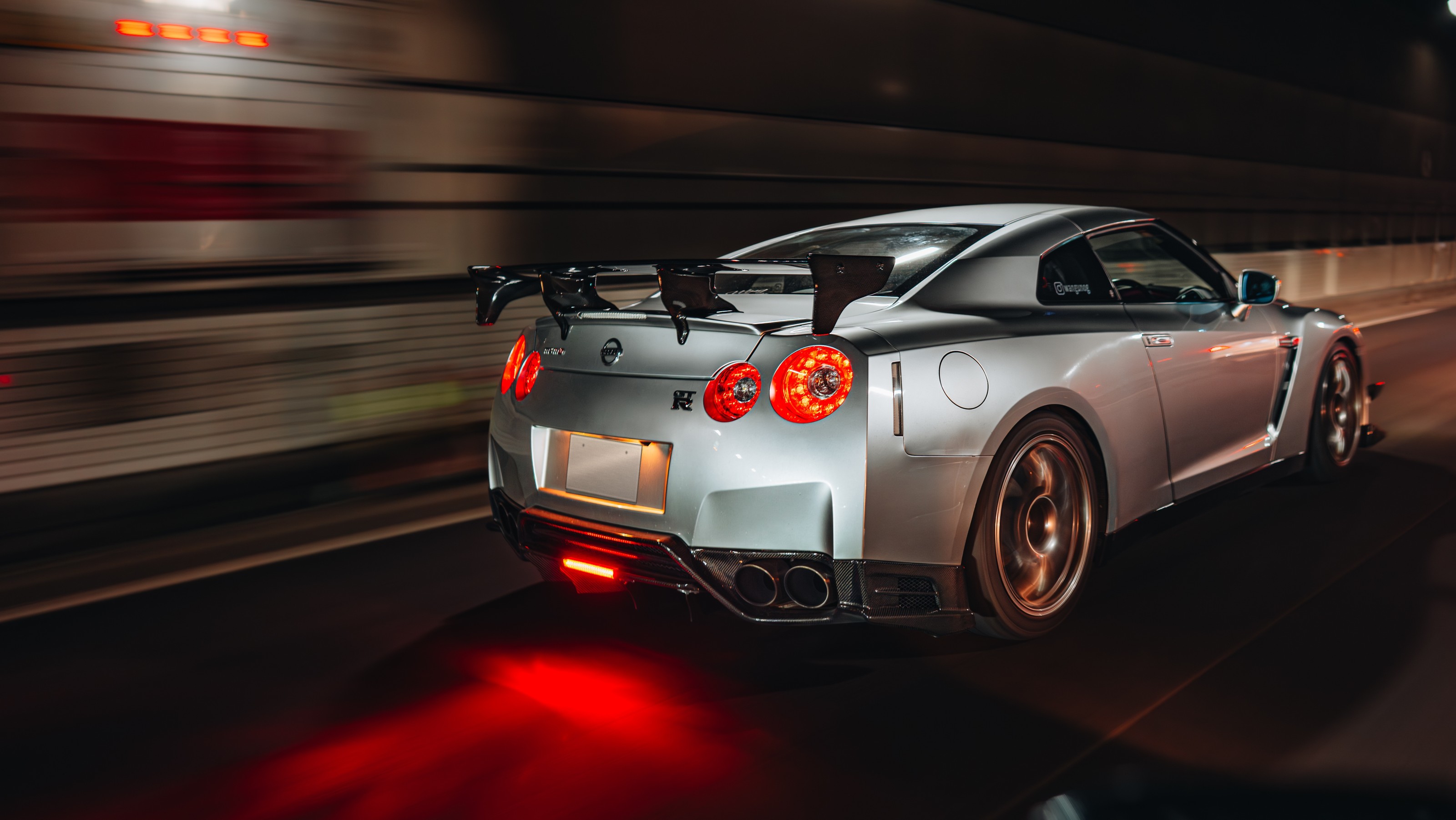 Silver Nissan GT-R R35 driving on the Tokyo expressway at night with its round tail lights glowing